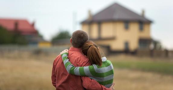 young-couple-hugging-eachother-looking-at-house-distance_573x300